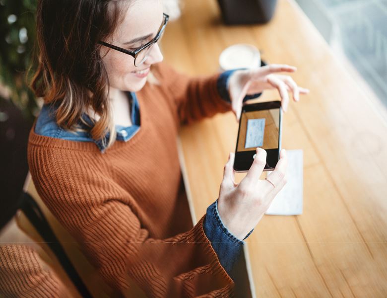 A girl using her phone to take a picture and deposit a check through the BOS Mobile App.