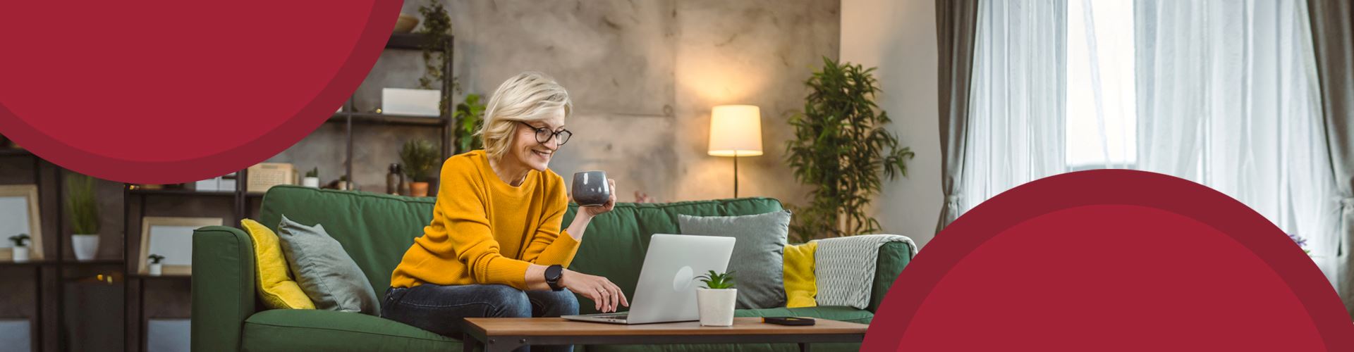 A woman sitting on the couch looking at her laptop and holding a coffee cup.