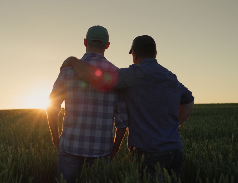 Two men standing in a field looking towards the sunset.